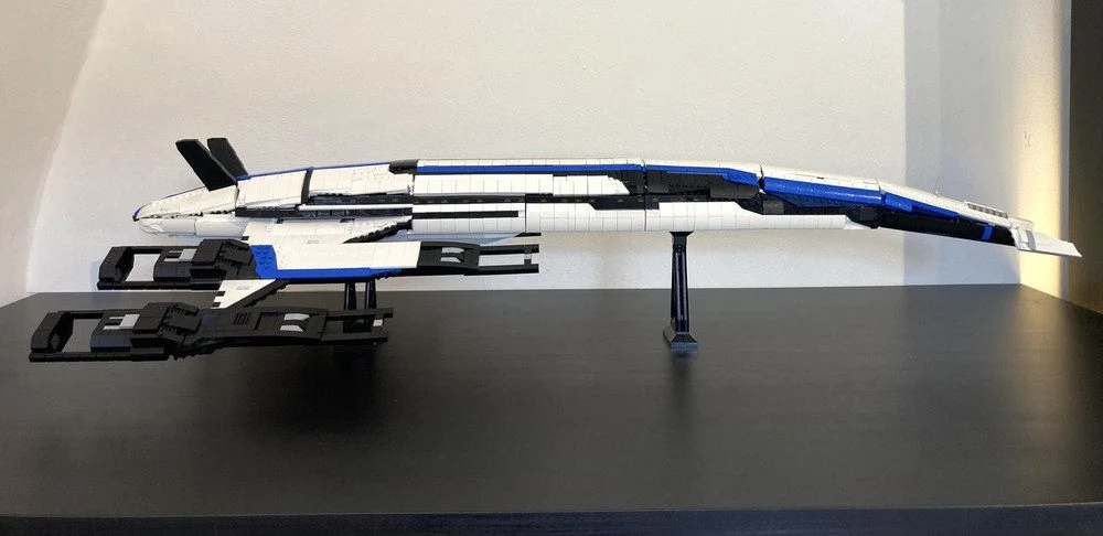 Lego Normandy SR-2 Model statku kosmicznego zbudowany z klocków, utrzymany w biało-czarno-niebieskiej kolorystyce, ustawiony na czarnej podstawce na tle jasnej ściany.