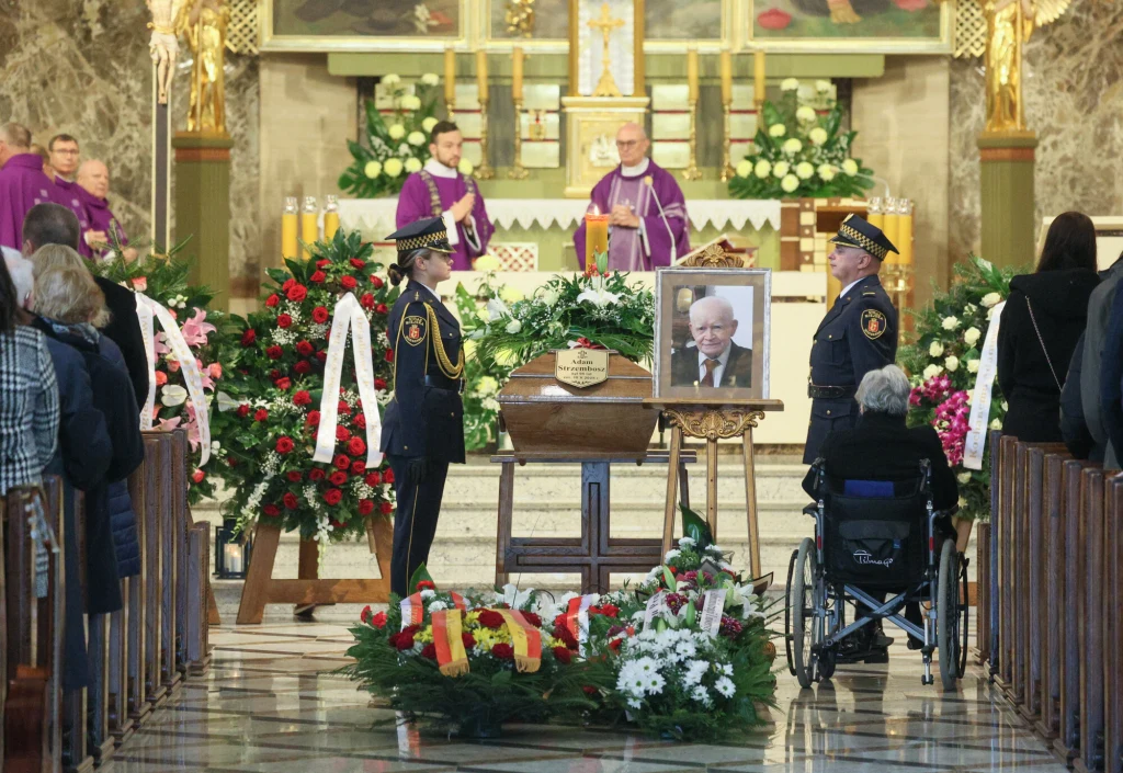 Pogrzeb prof. Adama Strzembosza Trumna z wieńcem oraz portretem zmarłego ustawiona na środku kościoła, wokół kwiaty i wieńce, przed trumną stoją honorowi żołnierze, z tyłu duchowni w fioletowych szatach liturgicznych prowadzą nabożeństwo, uczestnicy ceremonii siedzą w ławkach, na pie...