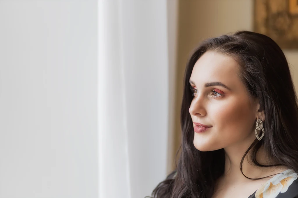 Ukryty potencjał znaków zodiaku. Tylko nieliczni potrafią go wykorzystać Młoda kobieta o długich, ciemnych włosach i wyrazistym makijażu spogląda przez okno, nosi eleganckie kolczyki i delikatnie się uśmiecha.