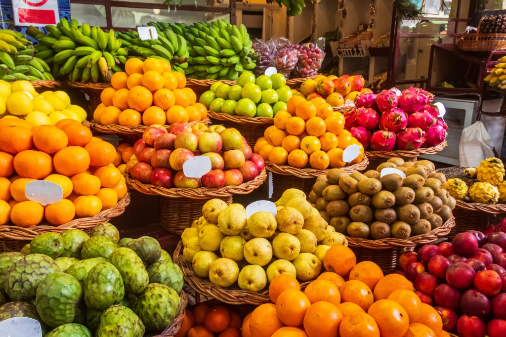 Nie jest łatwo kupić ceriman w Polsce Kosze wypełnione różnorodnymi owocami egzotycznymi i lokalnymi, takimi jak banany, jabłka, kiwi, ananasy, cytrusy oraz liczi, ustawione piętrowo na stoisku targowym.