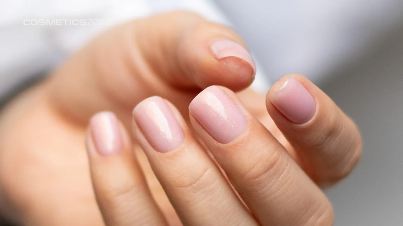 Delikatna hybrydowa baza hipoalergiczna Cosmetics Zone pięknie się mieni i zapewnia naturalny wygląd płytki Zadbane dłonie z krótkimi paznokciami pokrytymi jasnoróżowym lakierem, lekko świecące powierzchnie paznokci i naturalny wygląd skóry.