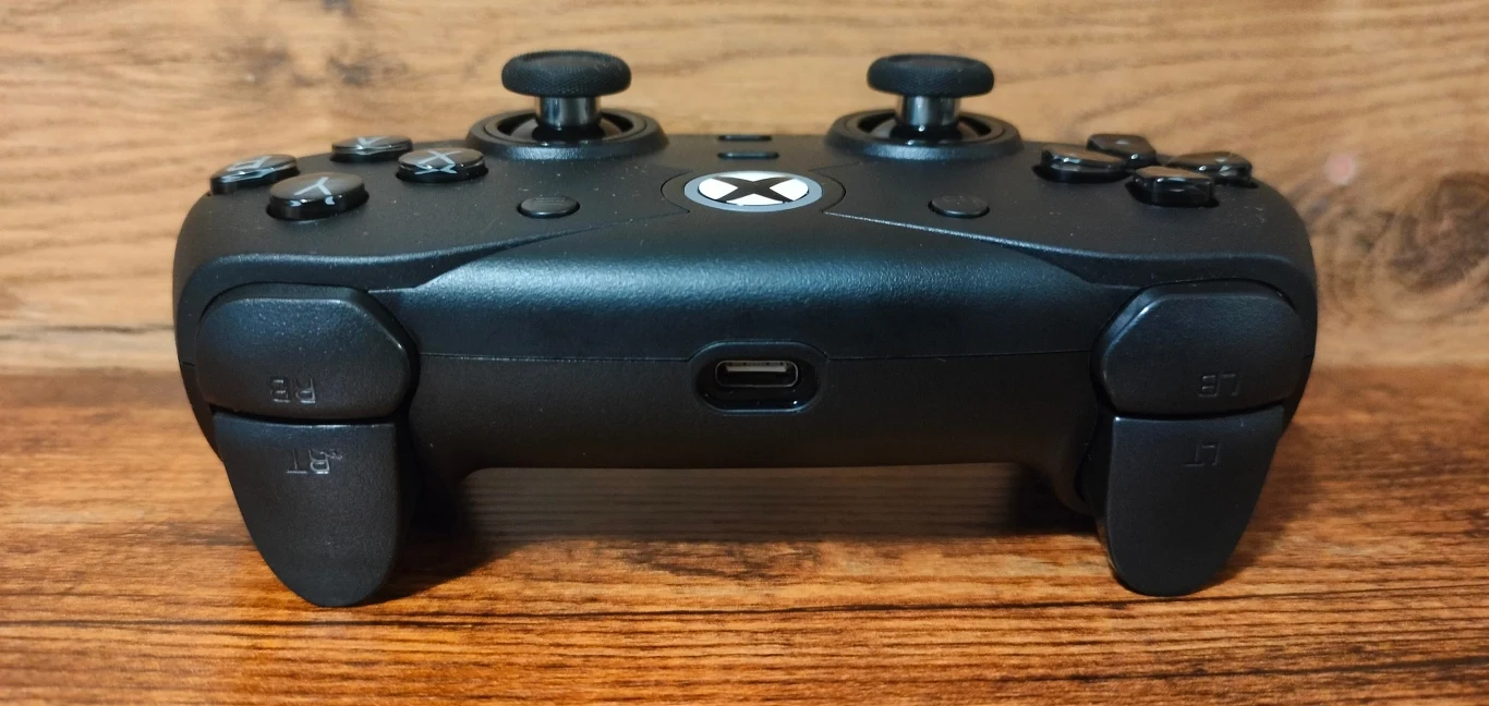 Czarny kontroler do konsoli Xbox ustawiony na drewnianej powierzchni, widoczne złącze USB typu C oraz przyciski z przodu urządzenia.