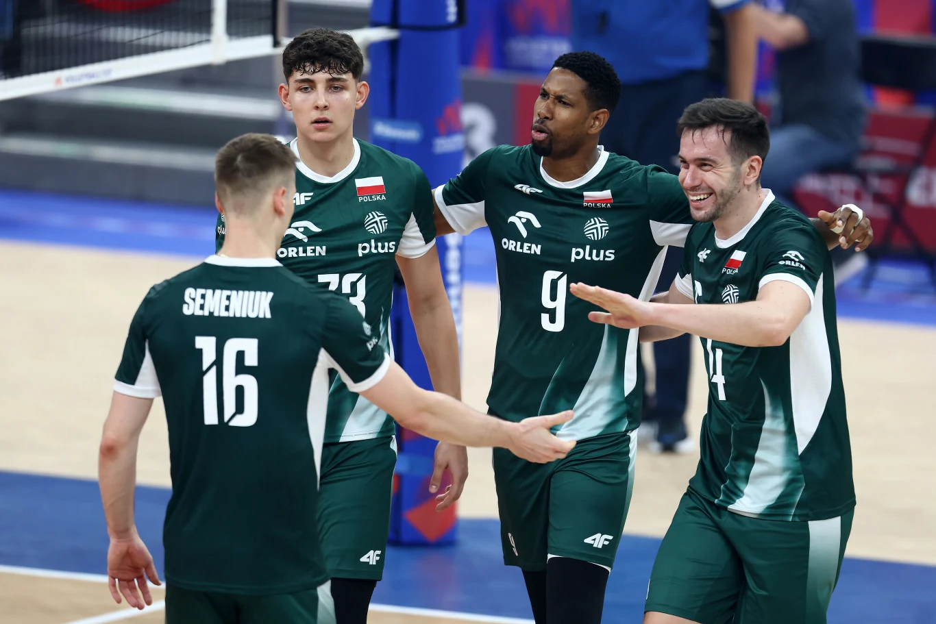 Zawodnicy męskiej reprezentacji Polski w siatkówce w zielonych strojach sportowych cieszą się wspólnie po udanej akcji na boisku. Widoczne są wyraźne emocje i radość, a w tle fragment siatki i parkietu.