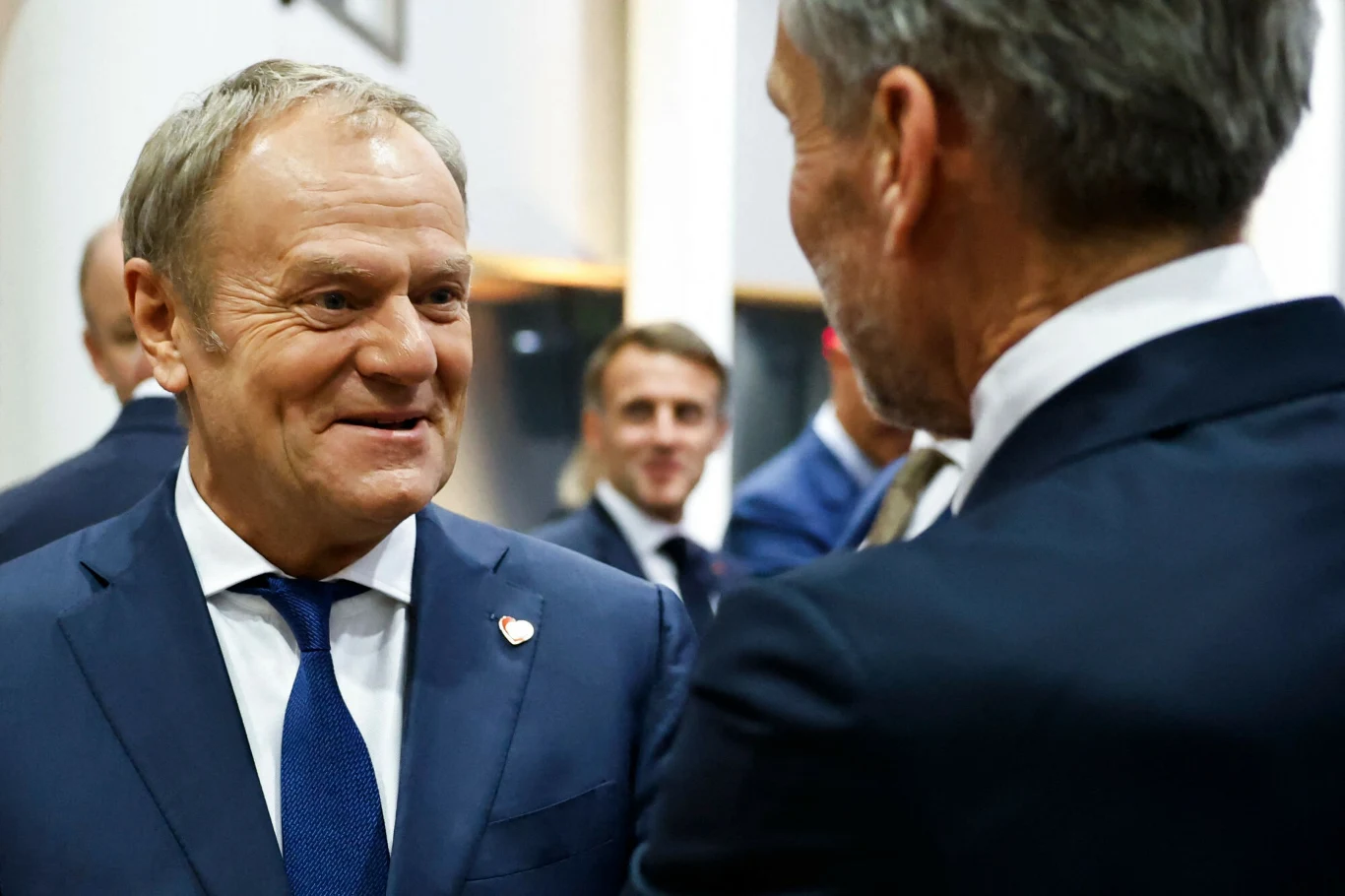 Tusk o przyszłości ETS2. "Usunęliśmy to zagrożenie" Mężczyzna w garniturze z przypinką na klapie prowadzi rozmowę z innym mężczyzną, w tle widoczni są kolejni uczestnicy spotkania w formalnych strojach