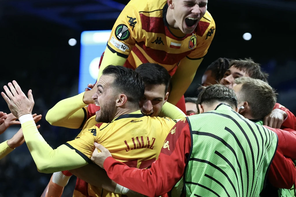 Jagiellonia fetuje objęcie prowadzenia na obiekcie RC Strasbourg Grupa piłkarzy w żółto-czerwonych strojach świętuje bramkę, jeden z zawodników wznosi ręce do góry, a inny znajduje się na plecach kolegi, wszyscy okazują silne emocje radości.