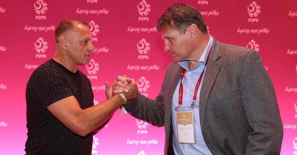 Piotr Świerczewski podczas niedawnego spotkania z Andrzejem Gołotą Dwóch mężczyzn ściska sobie dłonie na tle różowej planszy z logiem PZPN i napisem 'Łączy nas piłka'; obaj patrzą na siebie poważnie, jeden ubrany w czarny t-shirt, drugi w marynarkę z identyfikatorem.