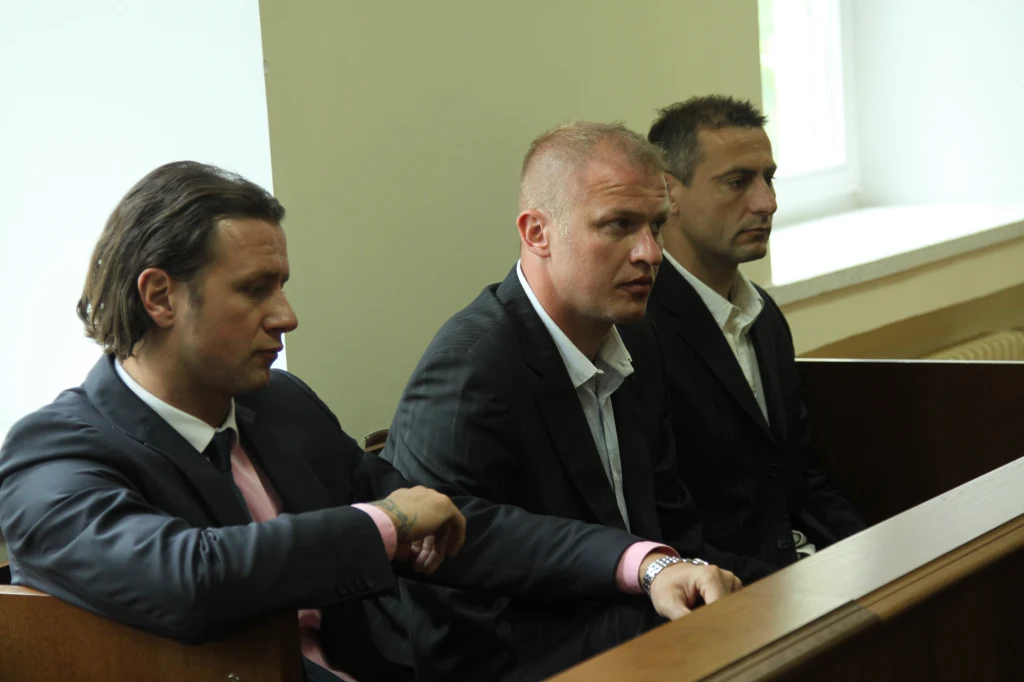 Sala sądowa, lato 2008 roku. Od lewej: Radosław Majdan, Jarosław Chwastek i Piotr Świerczewski Trzech mężczyzn w garniturach siedzących obok siebie na ławie sądowej, skupionych i poważnych, w tle jasne okno i jasne ściany sali sądowej.