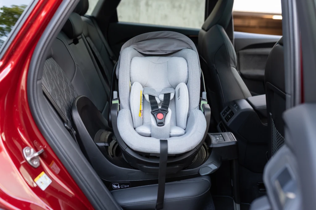Fotelik dziecięcy Thule Maple z jasnym obiciem zamontowany na tylnym siedzeniu czerwonego samochodu, wnętrze pojazdu widoczne z otwartymi drzwiami.
