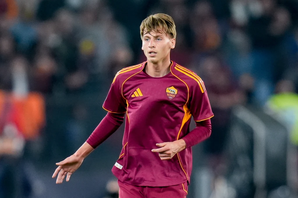 Jan Ziółkowski Młody piłkarz ubrany w bordowo-żółty strój drużyny AS Roma podczas meczu na stadionie, na tle rozmytej publiczności.