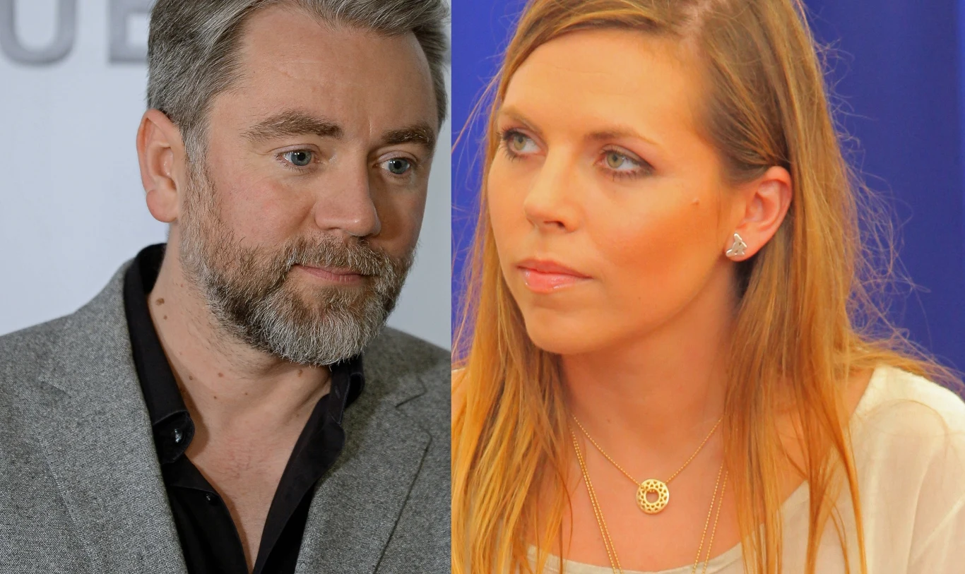 Kuba Badach i Aleksandra Kwaśniewska Dwie osoby, mężczyzna w siwym garniturze z brodą i kobieta z długimi blond włosami oraz delikatnym makijażem, siedzące obok siebie i patrzące w różne strony na neutralnym tle.