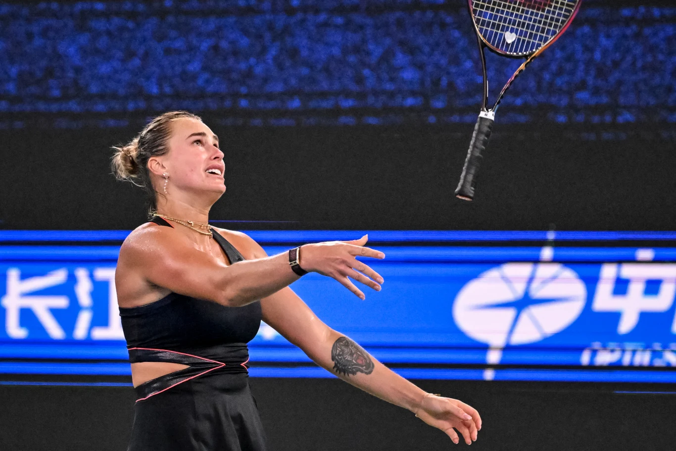 Aryna Sabalenka Zawodniczka tenisowa ubrana w czarny strój sportowy wyrzuca rakietę w powietrze, na jej twarzy widoczna jest emocja. W tle widać elektroniczną tablicę z napisami po chińsku.