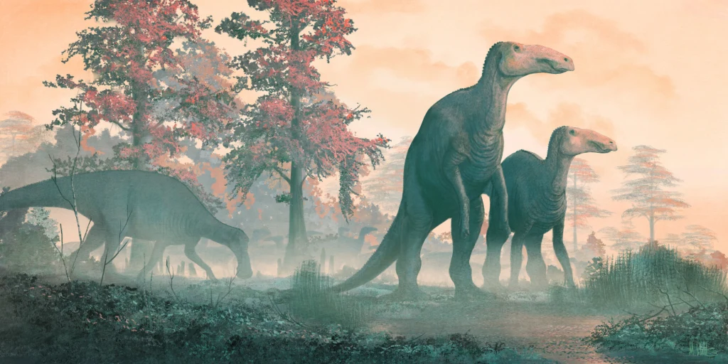 Edmontozaury były liczne pod koniec kredy Trzy duże dinozaury poruszają się po zamglonym, zalesionym terenie, wśród wysokich drzew z czerwonymi liśćmi, przy lekko zachmurzonym, różowawym niebie.