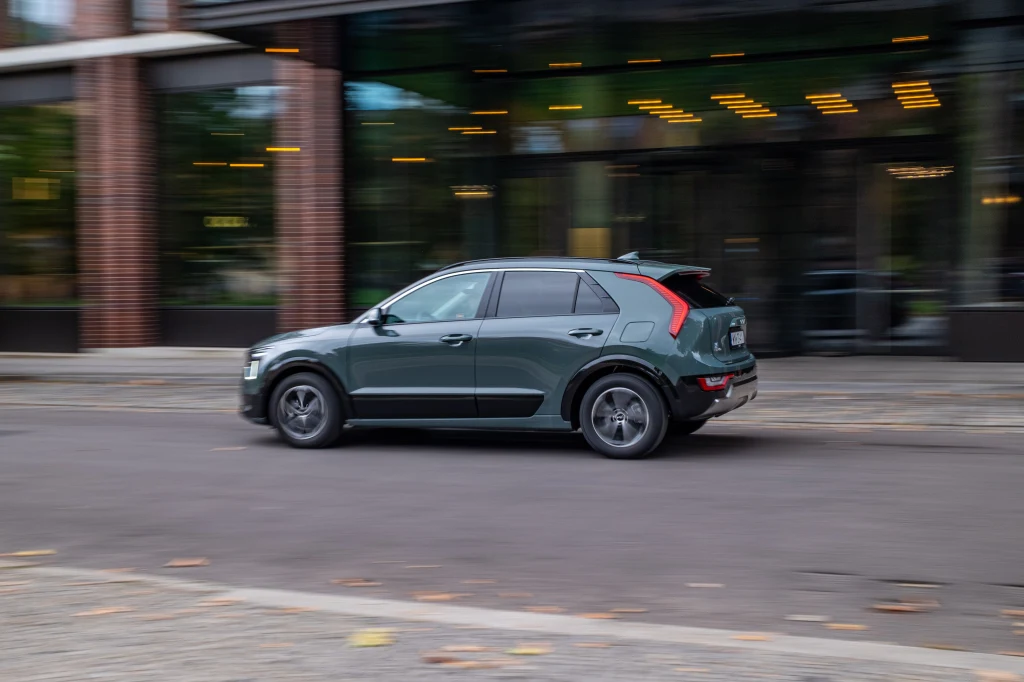 Zielony samochód typu SUV poruszający się po ulicy miasta, w tle widać fragment nowoczesnego budynku z przeszklonymi drzwiami oraz elementy zieleni.