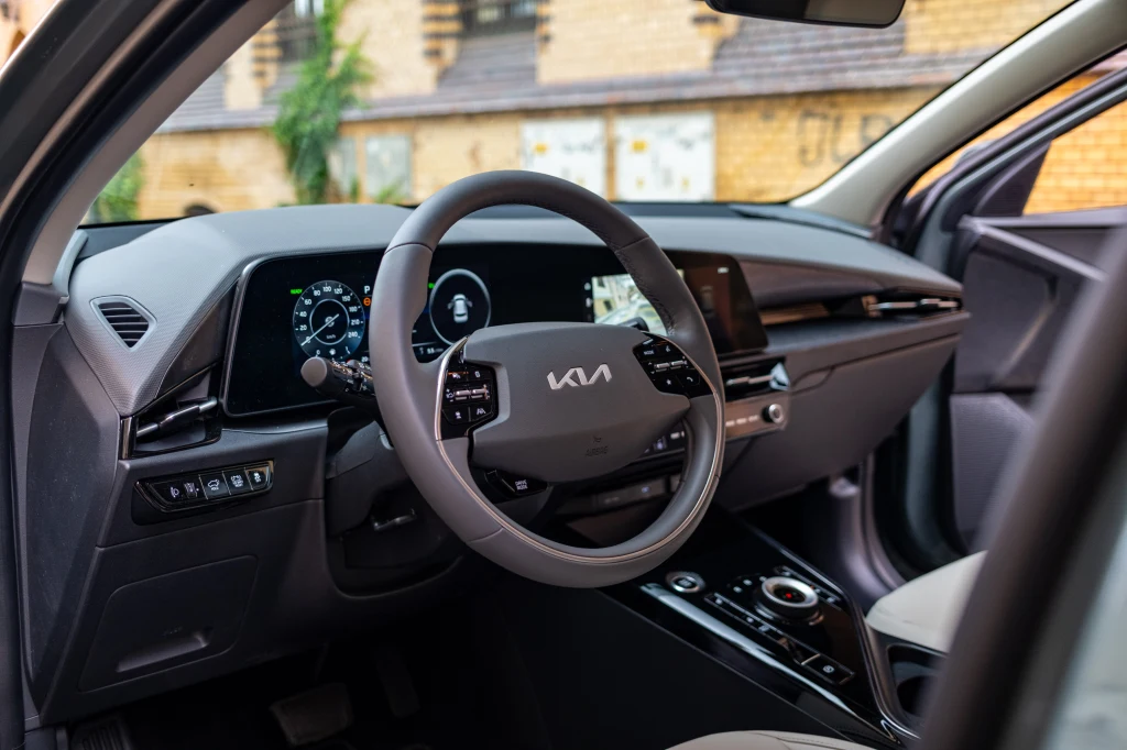 Nowoczesna deska rozdzielcza samochodu KIA z cyfrowymi wyświetlaczami, wielofunkcyjną kierownicą i designerską konsolą środkową, widocznymi detalami tapicerki oraz elementami elektrycznego sterowania.
