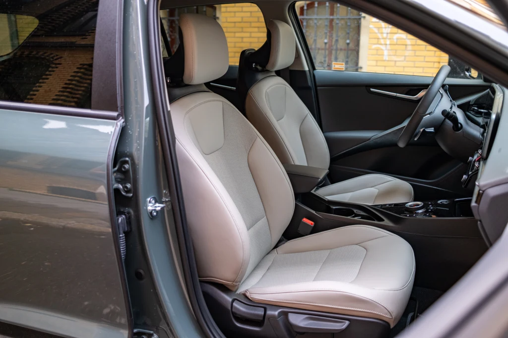 Wnętrze samochodu z otwartymi drzwiami po stronie kierowcy, dwa jasne fotele przednie, czarne elementy wykończenia oraz widoczna część deski rozdzielczej.