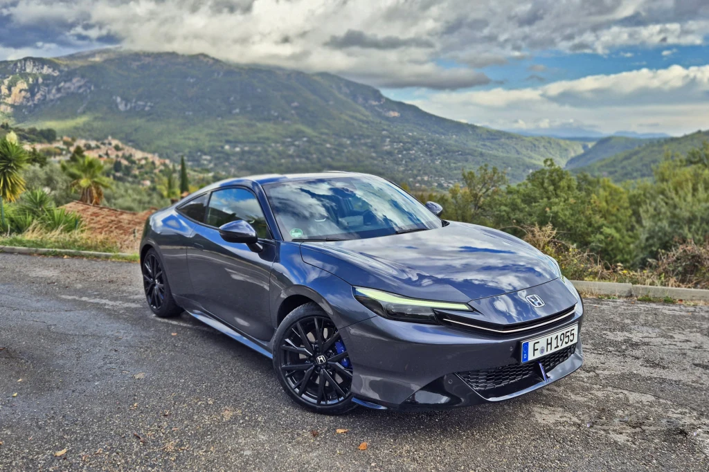 Honda Prelude zaskakująco dobrze radzi sobie na górskich drogach Sportowy samochód osobowy w kolorze grafitowym zaparkowany na poboczu drogi, w tle panoramiczny widok na góry oraz gęsta zieleń.