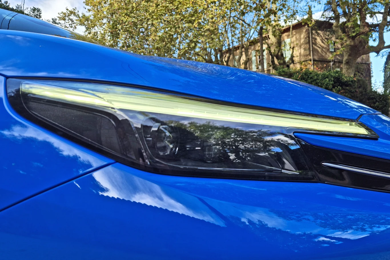 Honda Prelude Przedni reflektor nowoczesnego, niebieskiego samochodu odbijający otoczenie i drzewa w błyszczącej karoserii, z widocznym światłem LED oraz liniami nadwozia podkreślającymi sportowy charakter pojazdu