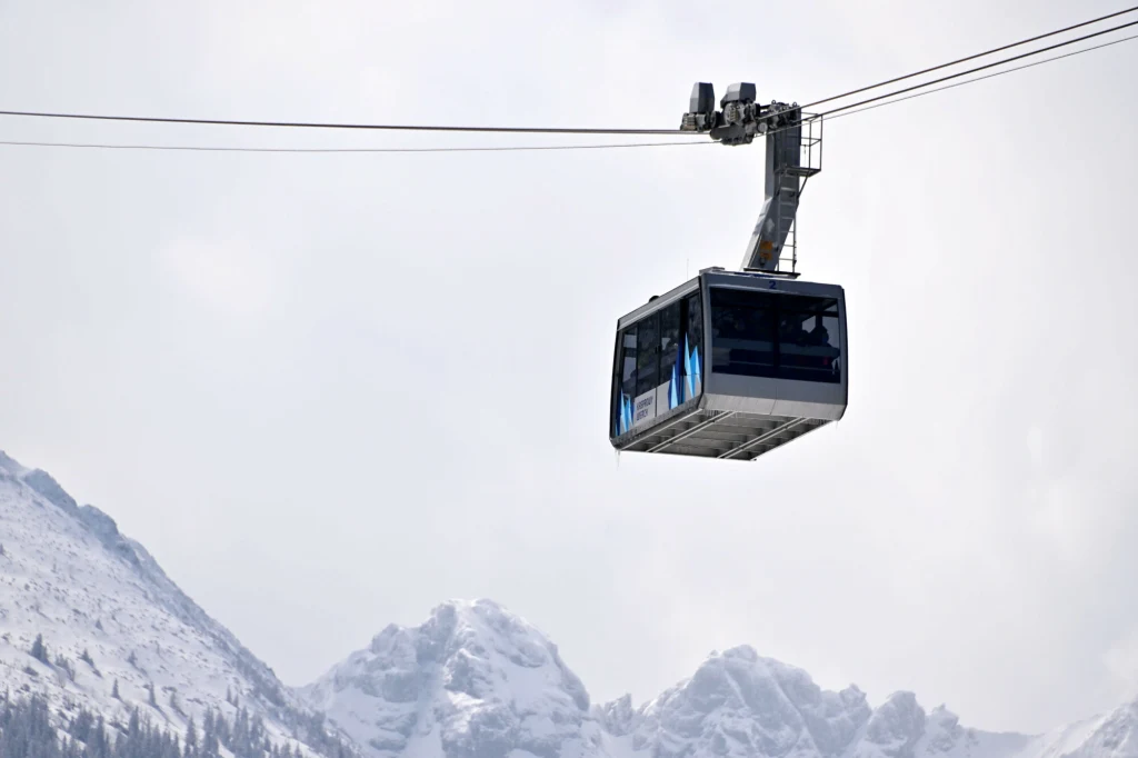 Kolejka linowa unosząca się nad ośnieżonymi szczytami górskimi w jasnym, zimowym krajobrazie.
