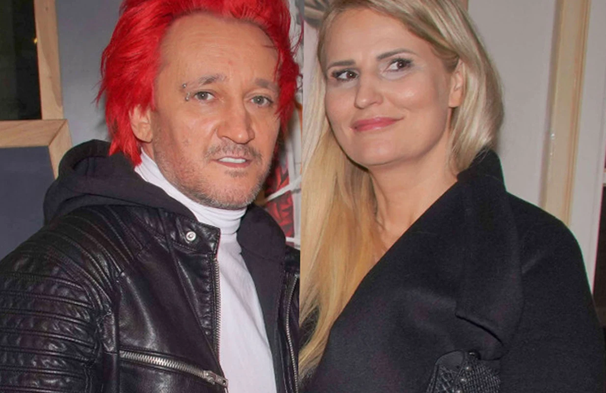 Dwie osoby pozujące razem, mężczyzna z intensywnie czerwonymi włosami w skórzanej kurtce i białym golfie oraz kobieta z długimi blond włosami w ciemnym płaszczu, na tle jasnych ścian wnętrza.