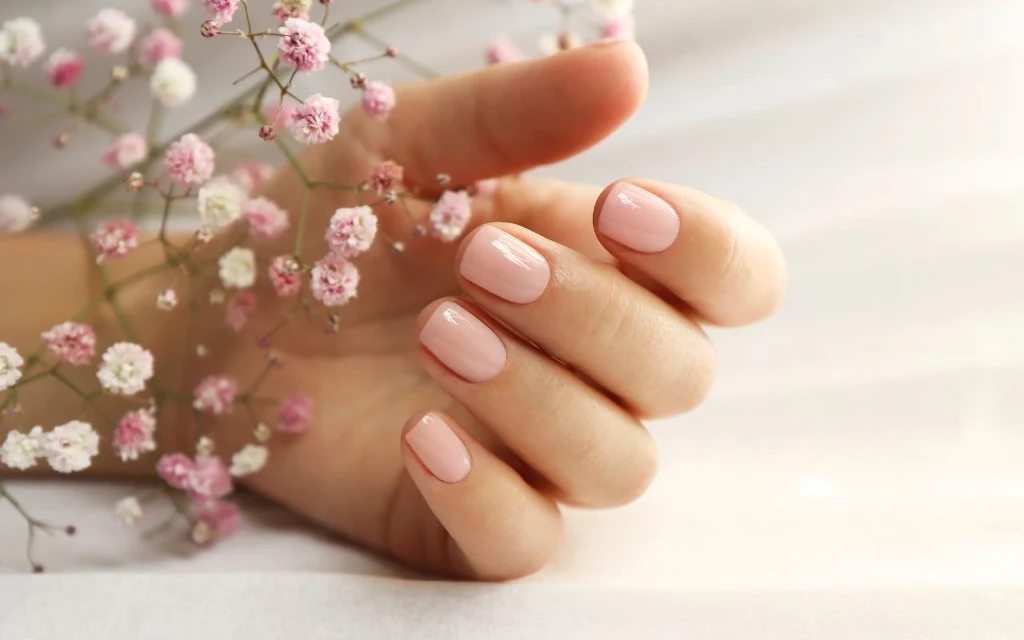 Ukraiński manicure podbija serca internautek. Pokochają gominimalistki Dłoń z zadbanymi paznokciami pomalowanymi jasnoróżowym lakierem otoczona drobnymi kwiatami gipsówki na jasnym tle.