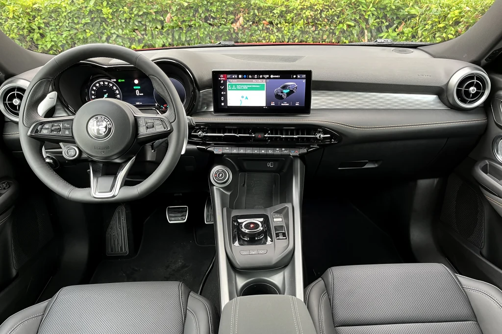 Nowoczesne wnętrze samochodu z cyfrowym wyświetlaczem centralnym, wielofunkcyjną kierownicą oraz elegancką deską rozdzielczą w czarnej kolorystyce, po bokach widoczne dwa fotele.