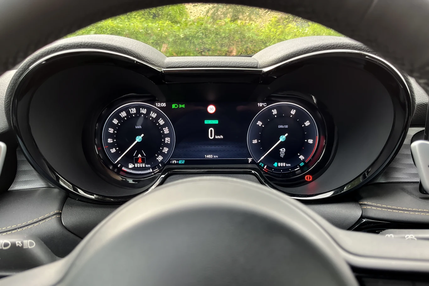 Cyfrowy panel wskaźników samochodu z prędkościomierzem, obrotomierzem i wyświetlaczem centralnym pokazującym aktualną prędkość, poziom paliwa oraz inne dane eksploatacyjne, otoczony elementami kierownicy.