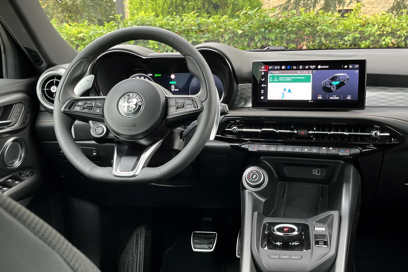 Kokpit nowoczesnego samochodu marki Alfa Romeo z cyfrowymi wyświetlaczami, skórzaną kierownicą, konsolą środkową z elektroniczną dźwignią zmiany biegów oraz ekranem dotykowym systemu multimedialnego.