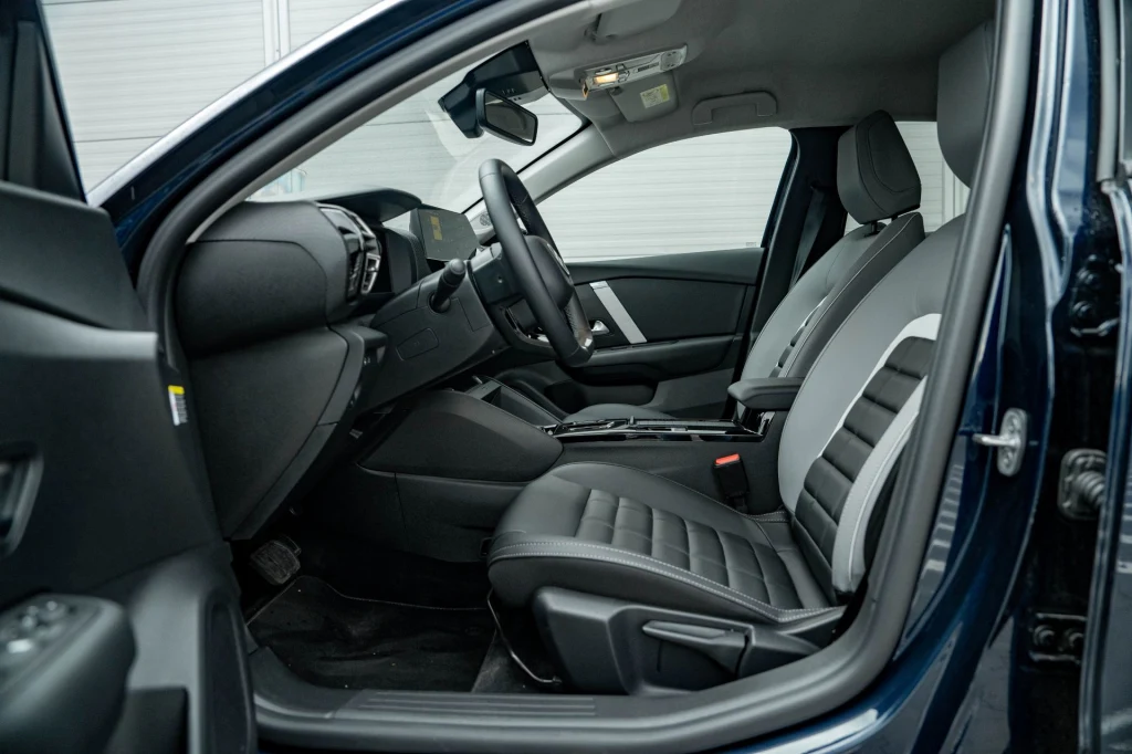 Widok nowoczesnego, czarno-szarego wnętrza samochodu osobowego obejmującego przednie siedzenia, deskę rozdzielczą oraz kierownicę, całość utrzymana w minimalistycznym stylu z dbałością o komfort i funkcjonalność.