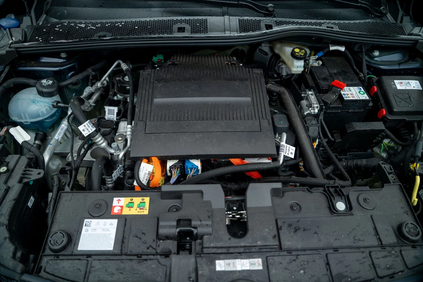 Komora silnika samochodowego z widocznymi przewodami, osłoną silnika oraz różnorodnymi komponentami elektronicznymi i zbiornikami płynów, utrzymana w czystości.