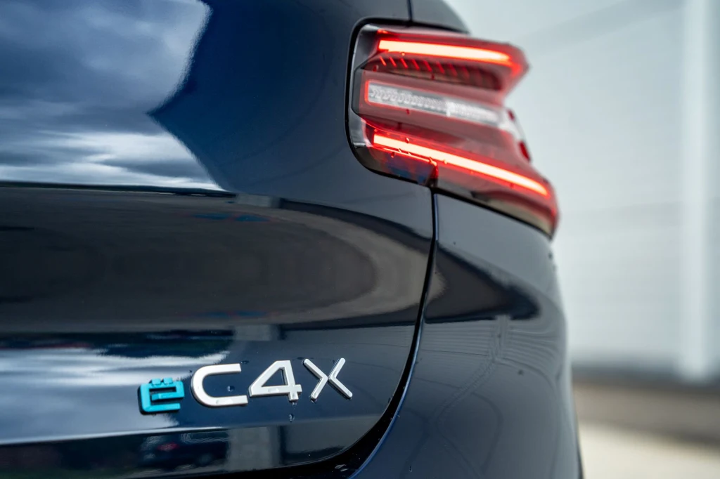 Elegancki fragment tyłu ciemnoniebieskiego samochodu Citroën ë-C4X z podkreślonym nowoczesnym tylnym światłem LED i emblematem modelu.