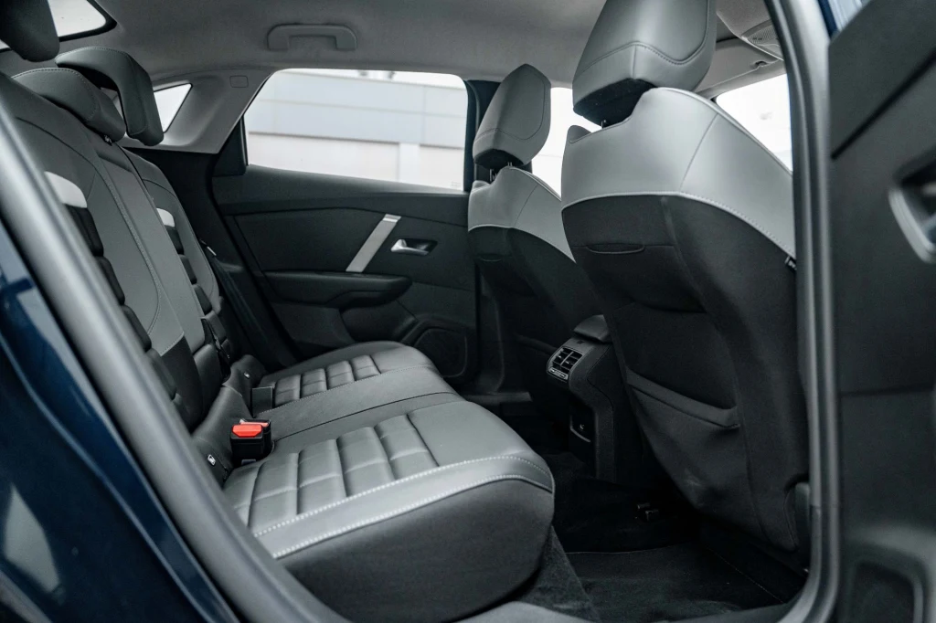 Wnętrze samochodu z widocznymi tylnymi siedzeniami, tapicerką z czarnej skóry oraz elementami nowoczesnego wykończenia, po obu stronach znajdują się drzwi, a pomiędzy siedzeniami wygodna ilość miejsca dla pasażerów.