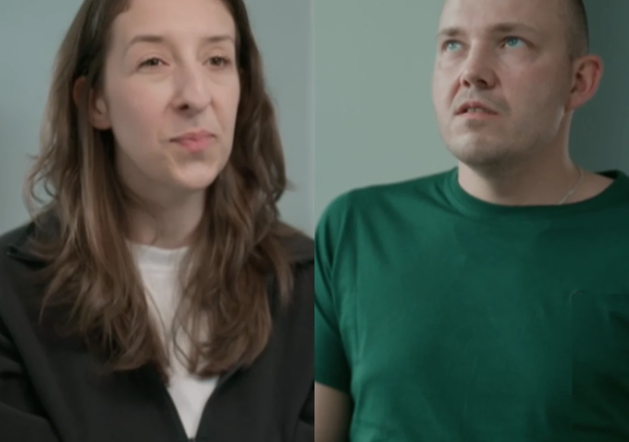 Kaja i Krystian ze "Ślub od pierwszego wejrzenia" Dwie osoby siedzące naprzeciwko siebie, kobieta o długich brązowych włosach w czarnym ubraniu i mężczyzna w zielonej koszulce, oboje na tle jasnej, neutralnej ściany.