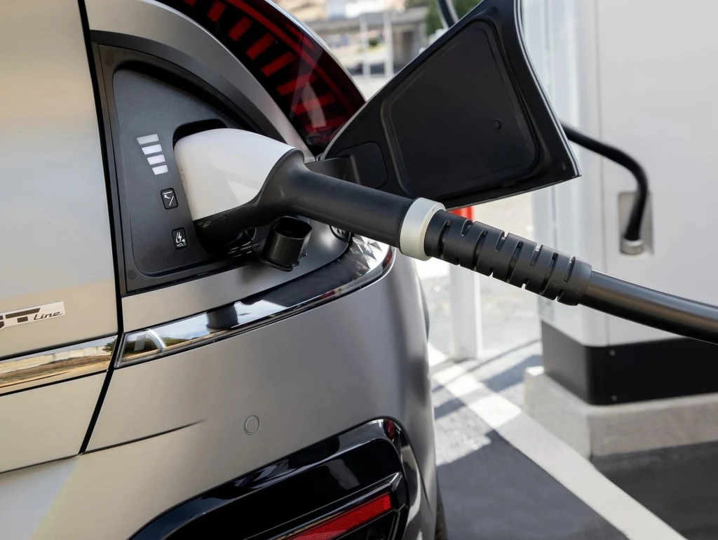 Ładowanie prądem wysokiej mocy prowadzi do szybszej degradacji akumulatora Zbliżenie na wtyczkę ładowarki podłączoną do portu elektrycznego samochodu podczas ładowania pojazdu na stacji.