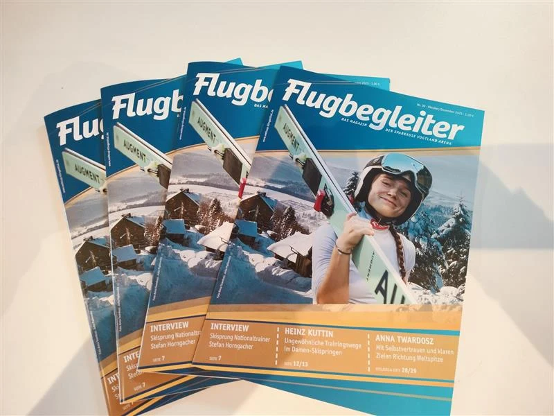 Anna Twardosz w magazynie "Flugbegleiter" Stos magazynów "Flugbegleiter" z zimową scenerią, skoczkiem narciarskim trzymającym narty i uśmiechającym się do aparatu na okładce, w tle góry oraz śnieżne dachy budynków.