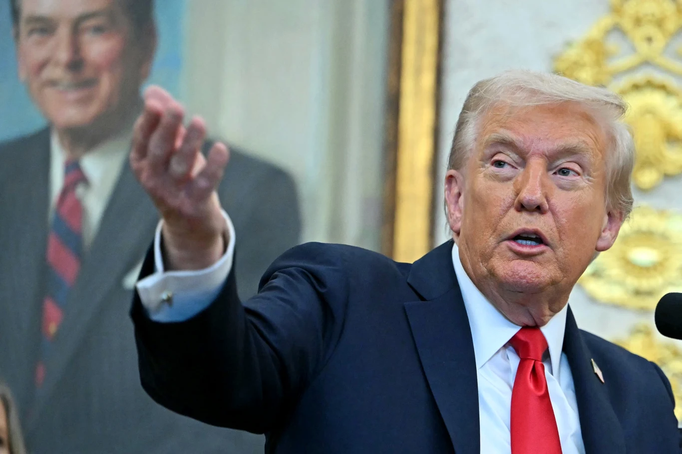 Donald Trump nałożył dodatkowe 10-procentowe cła na import z Kanady Mężczyzna w garniturze i czerwonym krawacie gestykuluje ręką, w tle widoczny jest portret innego mężczyzny ubranej w garnitur i krawat.