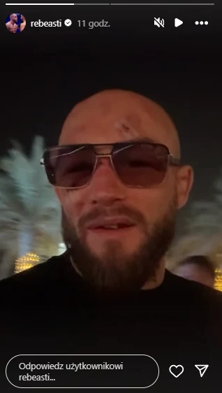 Mateusz Rębecki po walce na UFC 321 Mężczyzna z brodą w okularach przeciwsłonecznych, widoczne zadrapania lub rany na czole, w tle nieostre palmy i światła nocne.