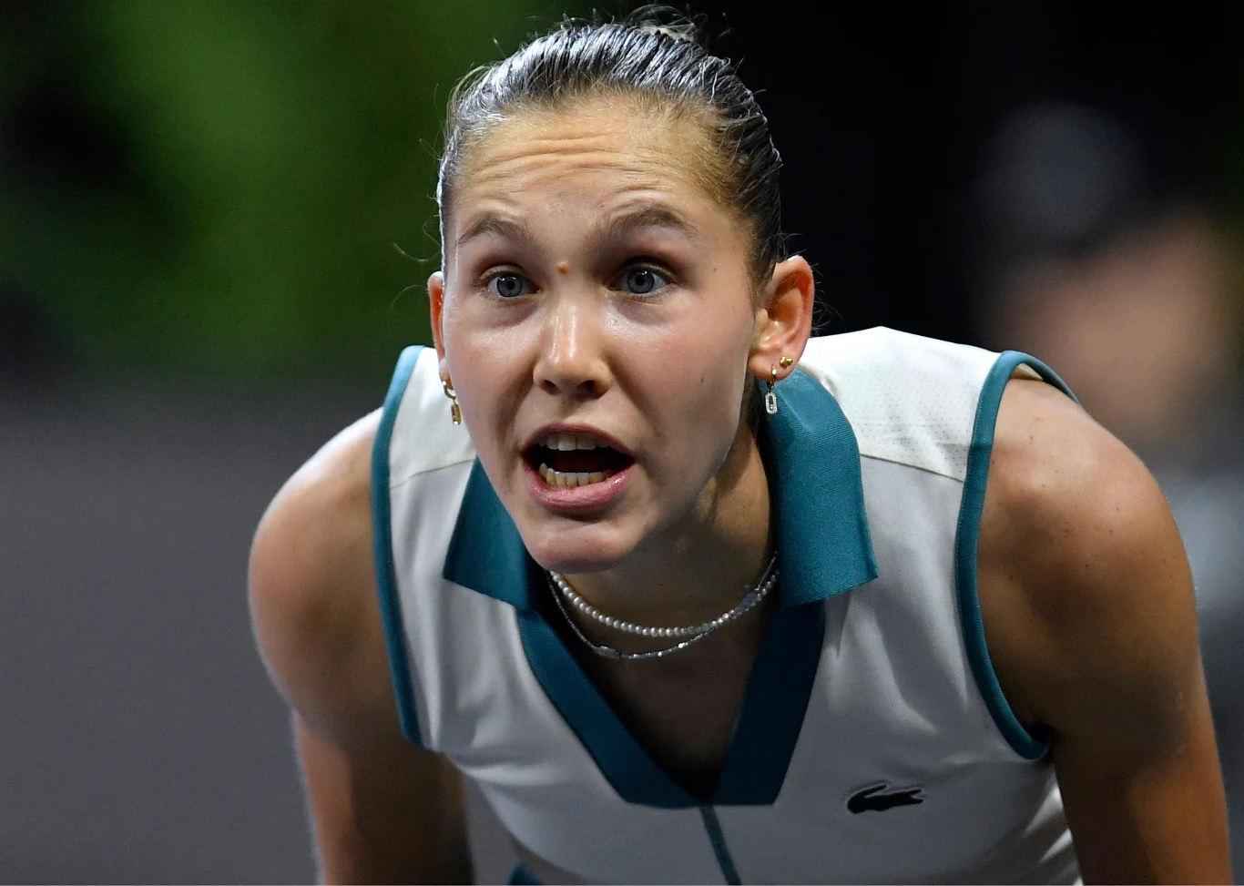 Młoda kobieta w sportowym stroju tenisowym pochylona i patrząca z intensywnym wyrazem twarzy, skóra błyszcząca od potu, tło rozmyte.