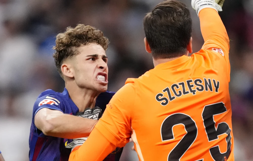 Fermin Lopez w ekspresyjny sposób gratuluje Wojciechowi Szczęsnemu obrony rzutu karnego Dwóch piłkarzy w sportowej rywalizacji, jeden z nich wyraża silne emocje chwytając drugiego za koszulkę, drugi w pomarańczowym stroju bramkarskim z widocznym nazwiskiem Szczęsny na plecach.