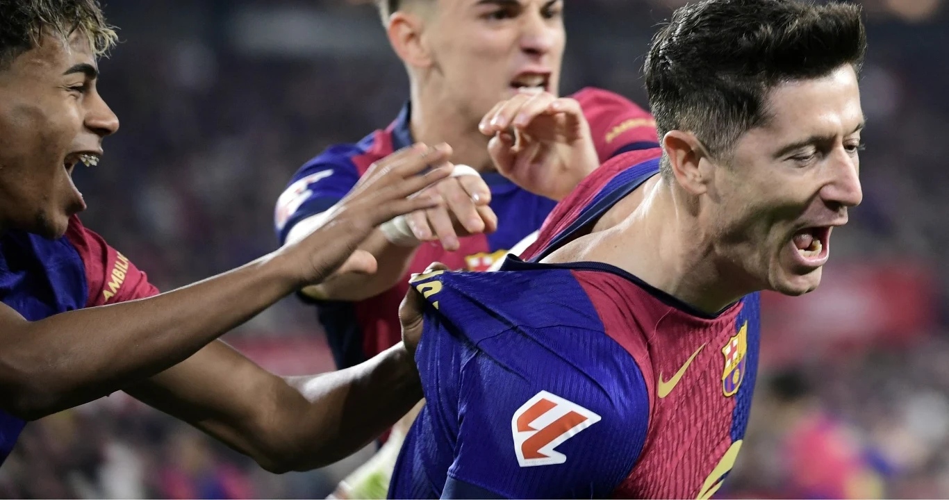 Piłkarz w koszulce FC Barcelony wyraża radość po zdobyciu gola, jego koledzy z drużyny entuzjastycznie okazują wsparcie, chwytając go za koszulkę, w tle rozmazana publiczność stadionu podkreśla atmosferę sportowej rywalizacji.