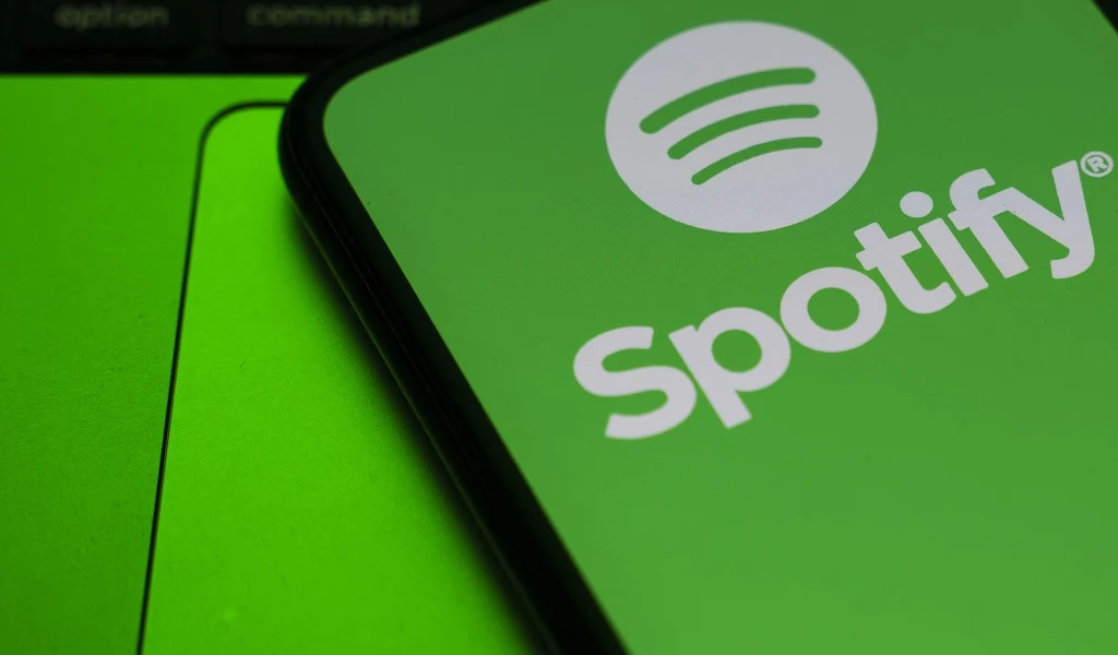Logo Spotify na ekranie telefonu komórkowego, telefon leży na jasnym, zielonym tle, tworząc wyrazisty kontrast z czarną ramką urządzenia.