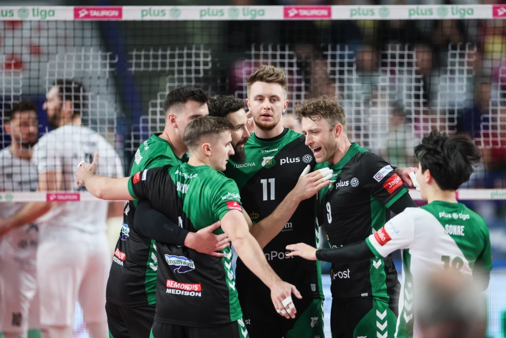 Siatkarze InPost ChKS Chełm pokonali Cuprum Stilon Gorzów Siatkarze w zielono-czarnych strojach świętują zdobycie punktu, stojąc razem przy siatce podczas meczu siatkarskiego PlusLigi, z drużyną przeciwną widoczną w tle.