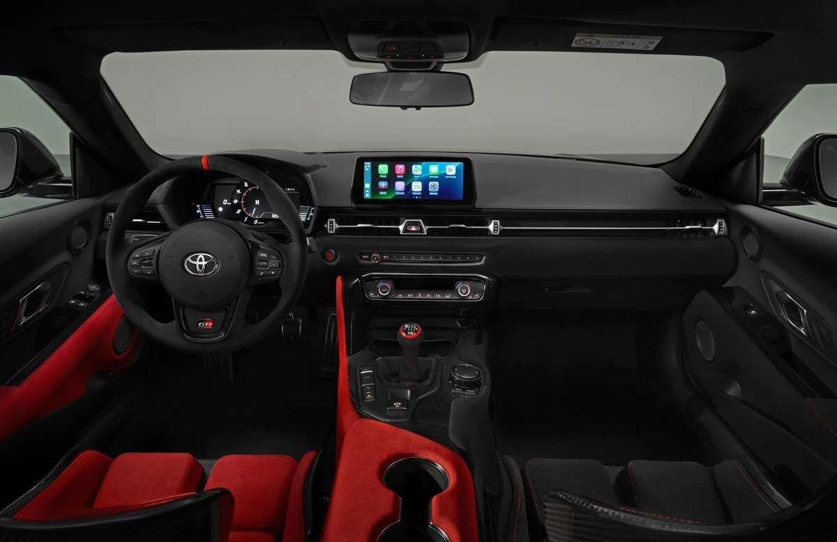 Toyota potwierdziła, że nie jest to definitywny koniec historii Supry. Kokpit sportowego samochodu marki Toyota z czerwono-czarnymi fotelami kubełkowymi, skórzaną kierownicą, cyfrowymi wskaźnikami oraz dużym wyświetlaczem multimedialnym na środku deski rozdzielczej.
