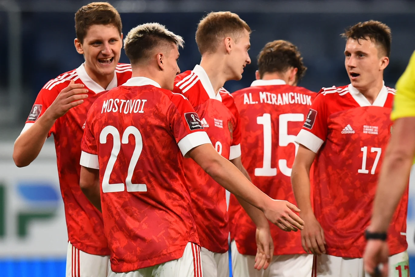 Grupa piłkarzy w czerwonych koszulkach świętuje wspólnie zdobycie gola na murawie stadionu, w tle widoczni są inni gracze oraz fragment trybun.