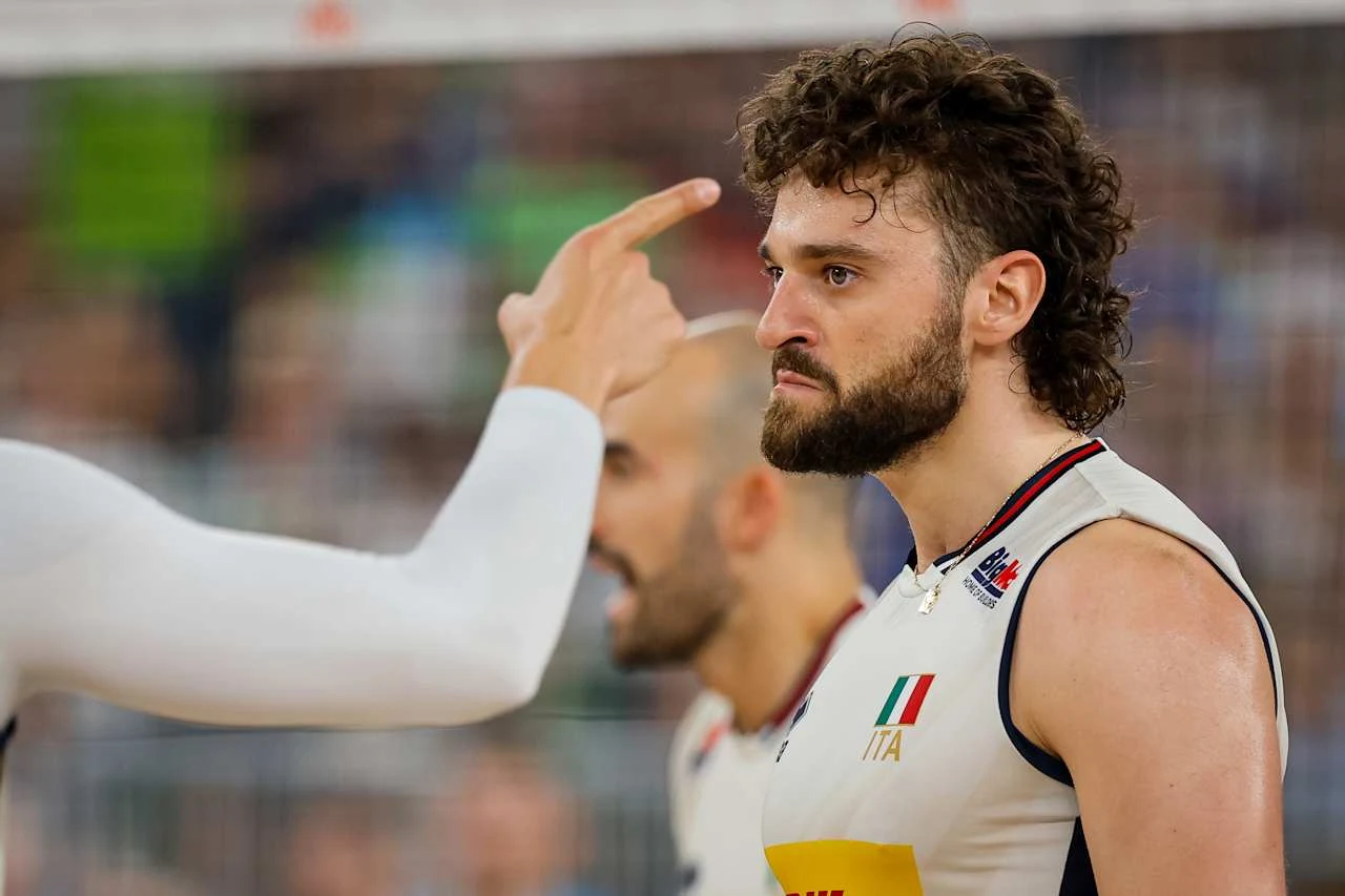 Męski zawodnik drużyny siatkarskiej z Włoch stoi z poważnym wyrazem twarzy, w jego kierunku wskazywany jest palec innego zawodnika, co sugeruje intensywną wymianę emocji podczas meczu.