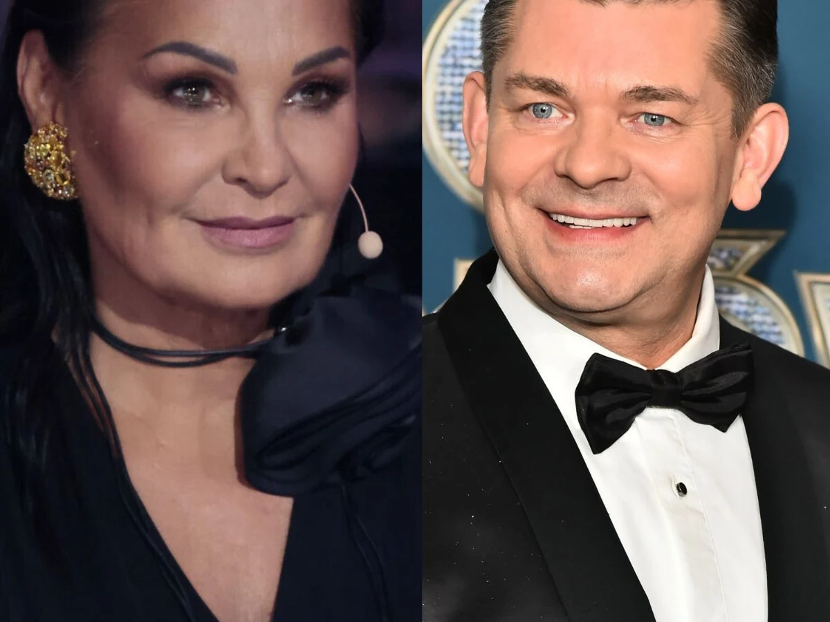 Dwie elegancko ubrane osoby, jedna w czarnym stroju z dużą złotą kolczyką i mikrofonem, druga w smokingu z muszką, obie uśmiechnięte, tło w odcieniach niebieskiego.