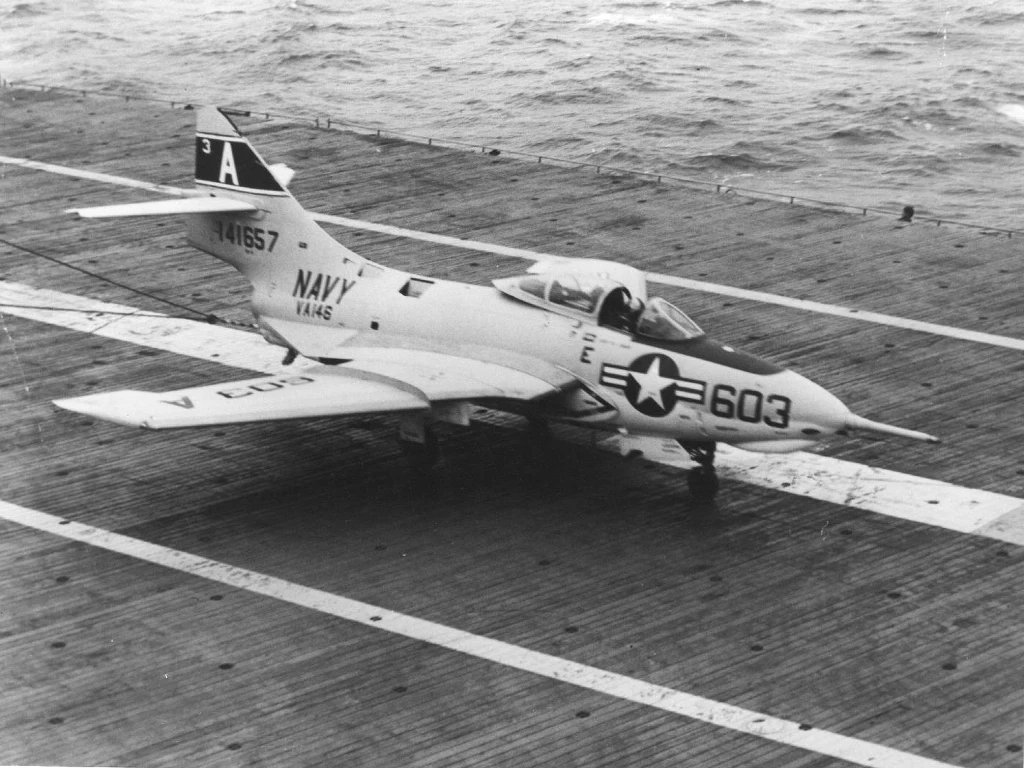 F9F Panther, był pierwszym samolotem odrzutowym, bazującym na amerykańskich lotniskowcach. Na zdjęciu jeden z samolotów na pokładzie USS Hornet w 1957 roku Wojskowy myśliwiec odrzutowy US Navy przygotowany do startu lub lądowania na pokładzie lotniskowca na tle oceanu. Samolot oznaczony numerem bocznym 603 oraz oznaczeniami marynarki wojennej.