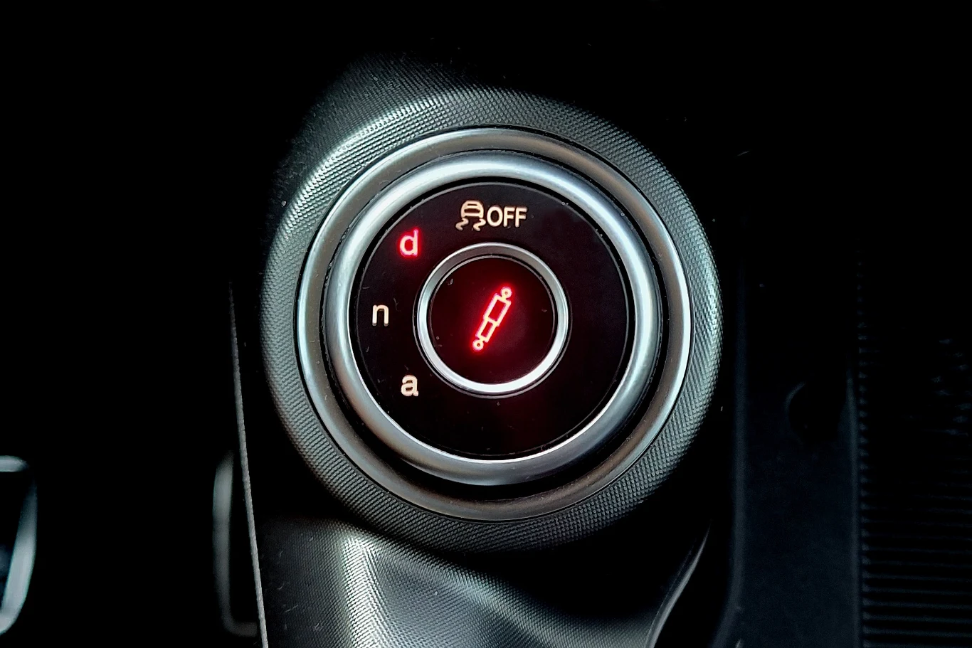 Panel sterowania skrzynią biegów oraz przyciskiem kontroli trakcji z podświetlonymi wskaźnikami trybów jazdy i symbolem pojazdu na czerwonym tle.