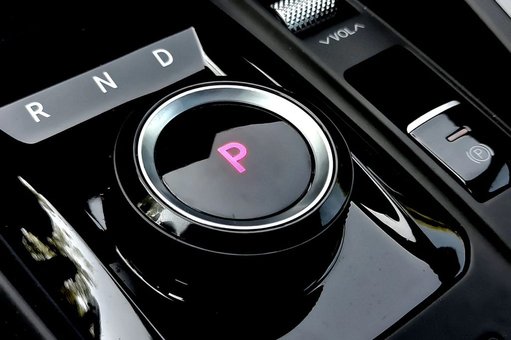 Pokrętło od sterowania skrzynią biegów. W Tonale po liftingu już go nie ma Centralnie umieszczony okrągły selektor automatycznej skrzyni biegów z wyraźnie widoczną literą P podświetloną na różowo oraz oznaczeniami trybów R, N, D. Obok selektora znajdują się przyciski dodatkowych funkcji, w tym przycisk hamulca postojowego.