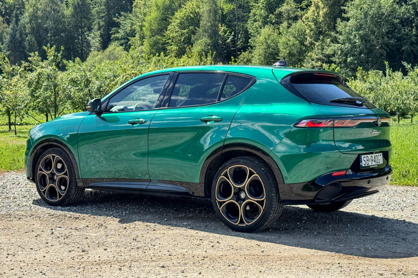 Zielony samochód typu SUV stoi na żwirowej drodze, w tle drzewa i zieleń, pojazd wyróżnia się nowoczesną sylwetką oraz czarnymi felgami z żółtymi akcentami.