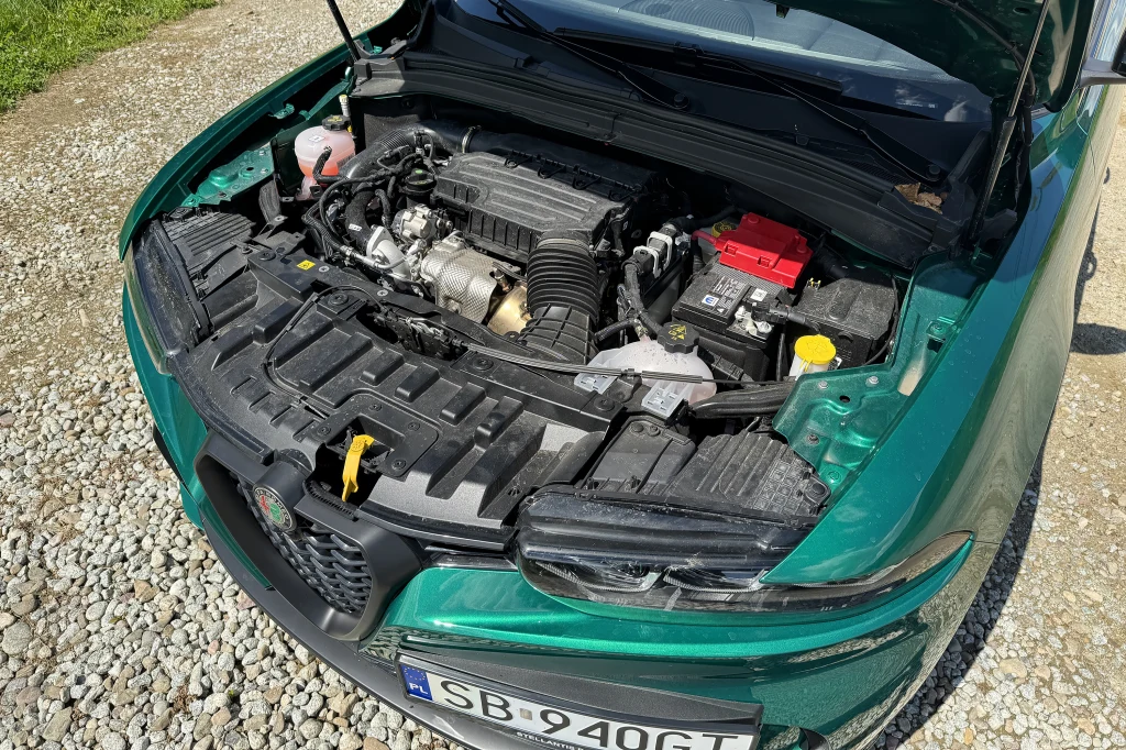 Napęd mikryhybrydowy opiera się o czterocylindrowy silnik 1.5 i generuje 160 KM Otwarte wnętrze komory silnika samochodu osobowego z widocznymi elementami mechanicznymi oraz akumulatorem, sfotografowane na żwirowej nawierzchni.